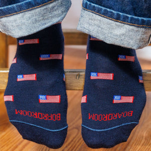 man sitting on a stool wearing jeans and american flag patterned merino wool dress socks