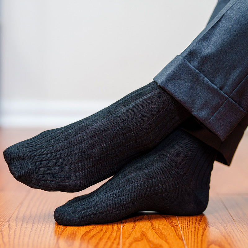 man wearing black ribbed dress socks crossing ankles with feet resting on hardwood floor
