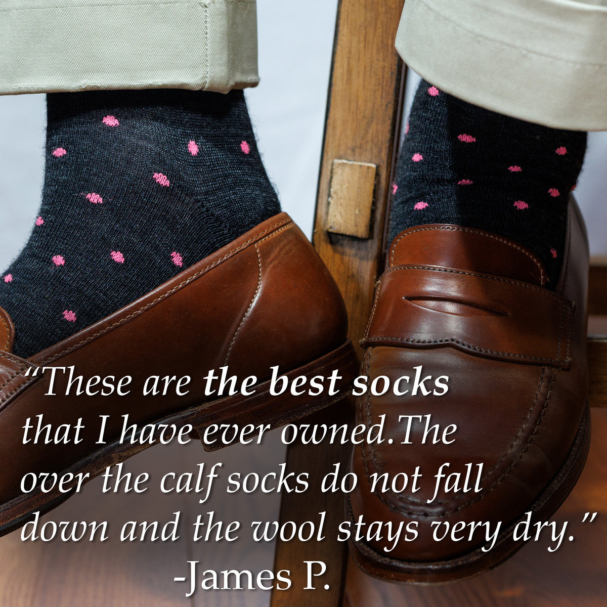 Person wearing charcoal dress socks with pink polka dots and brown penny loafers, sitting on a wooden chair.