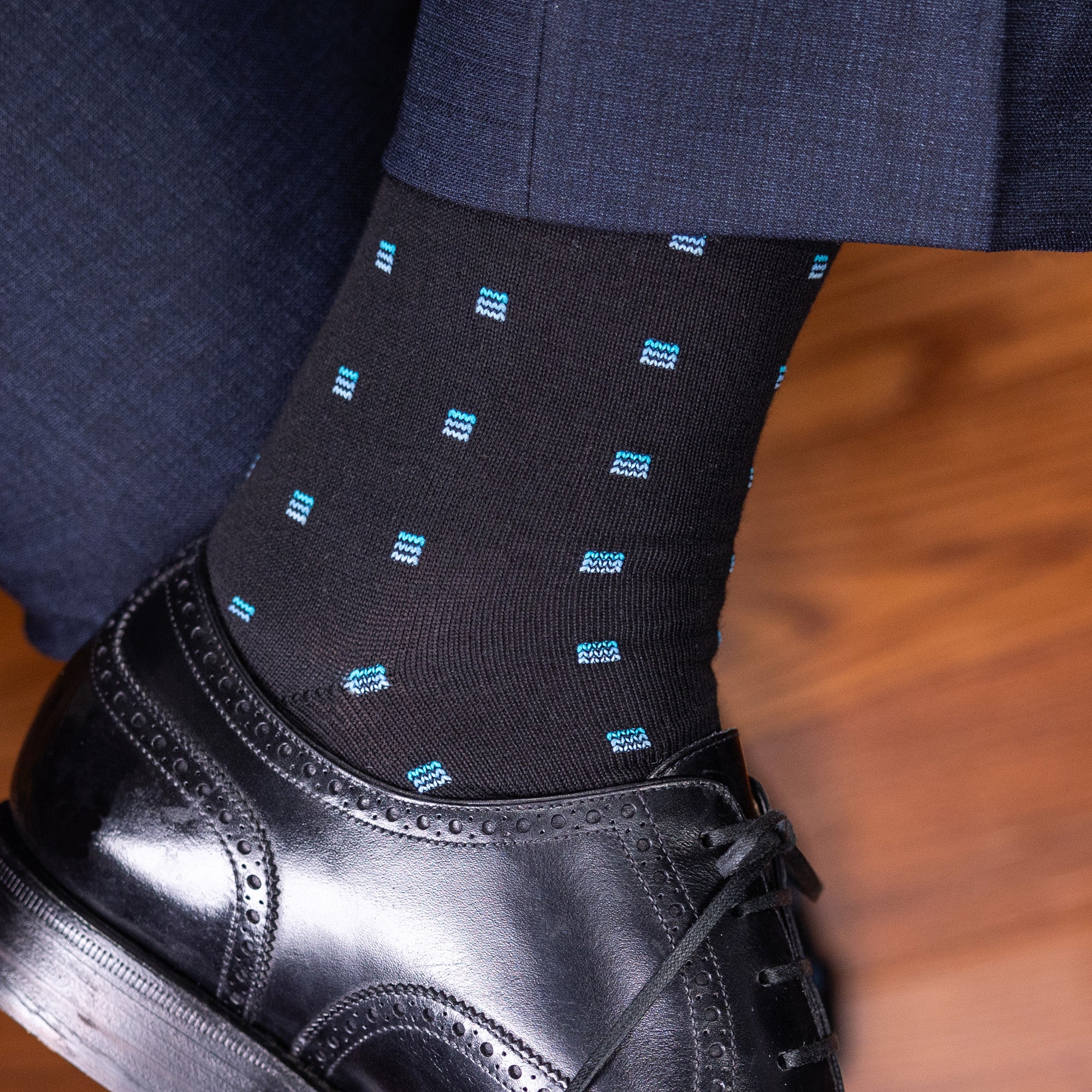man crossing ankles showing black cotton dress socks with unique blue geometric pattern