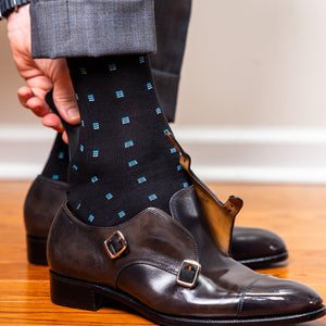 man sliding on monkstrap shoes with a shoe horn while wearing black and blue patterned dress socks