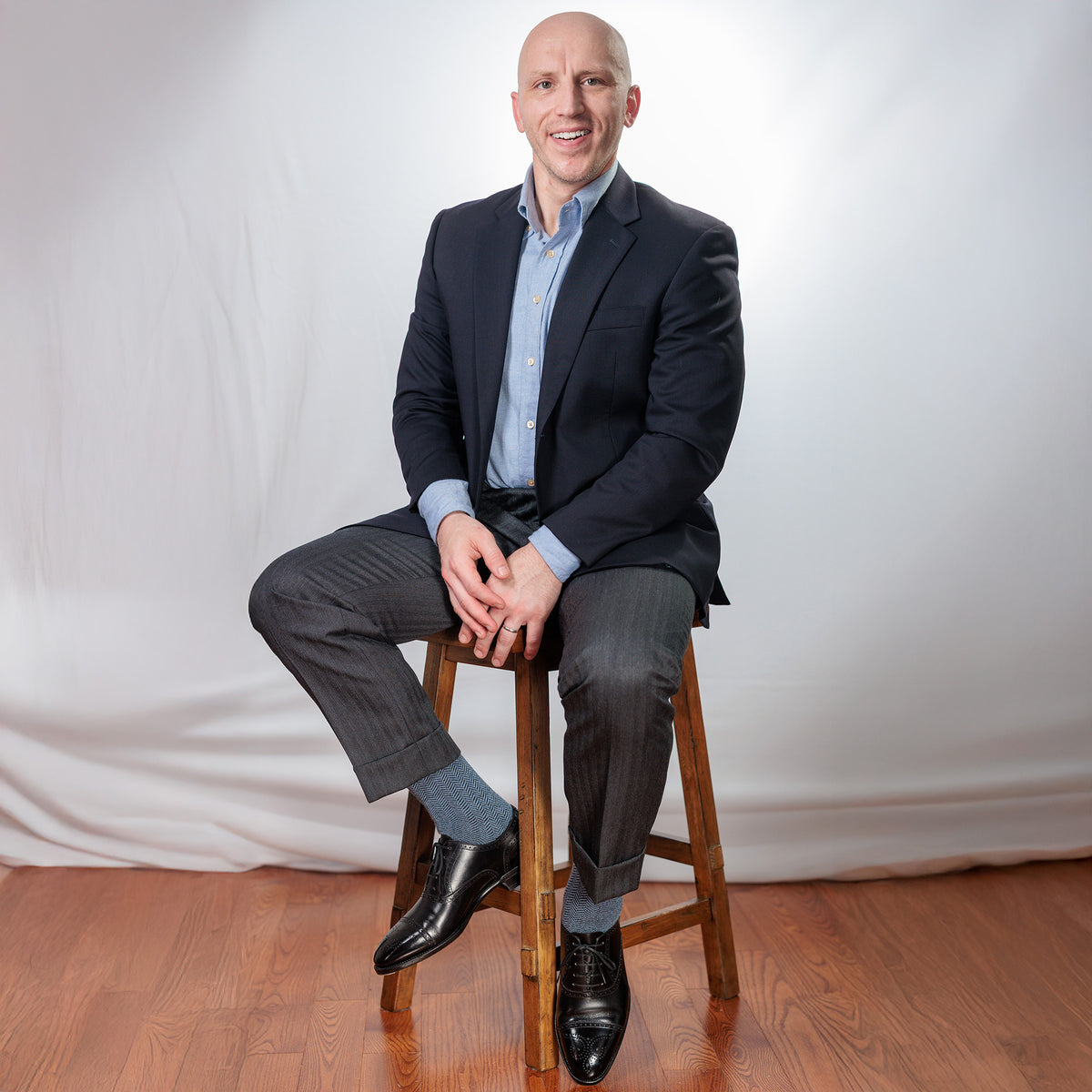 man wearing light blue and black herringbone dress socks with business casual attire sitting on stool