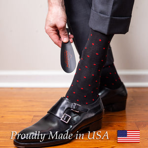 man wearing black patterned dress socks with bright red polka dots using shoe horn to put on black monkstrap shoes