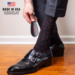 man wearing black cotton dress socks decorated with red polka dots using shoe horn to slide on black monkstrap shoes