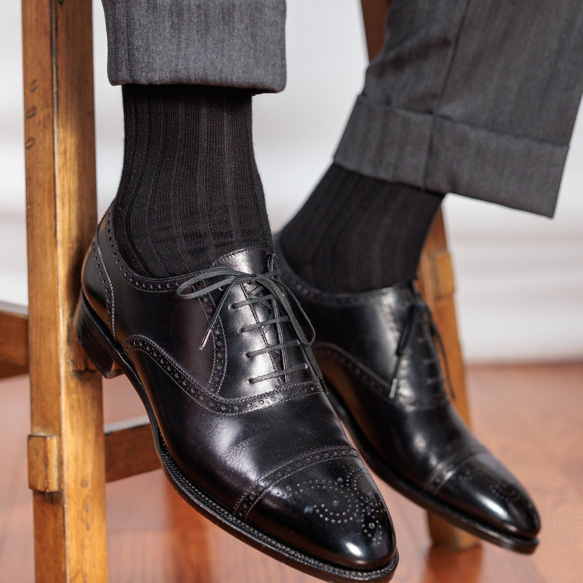 black cotton ribbed dress socks with grey slacks and black oxfords sitting on stool