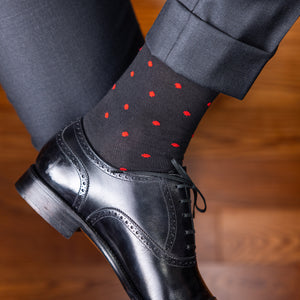 man wearing black cotton dress socks with red polka dots crossing ankles with charcoal suit