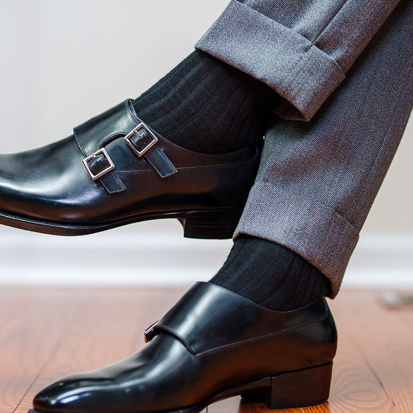 man crossing legs wearing black dress socks with monkstrap shoes and grey slacks