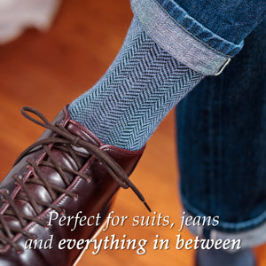 man crossing legs wearing light blue and black herringbone dress socks with jeans