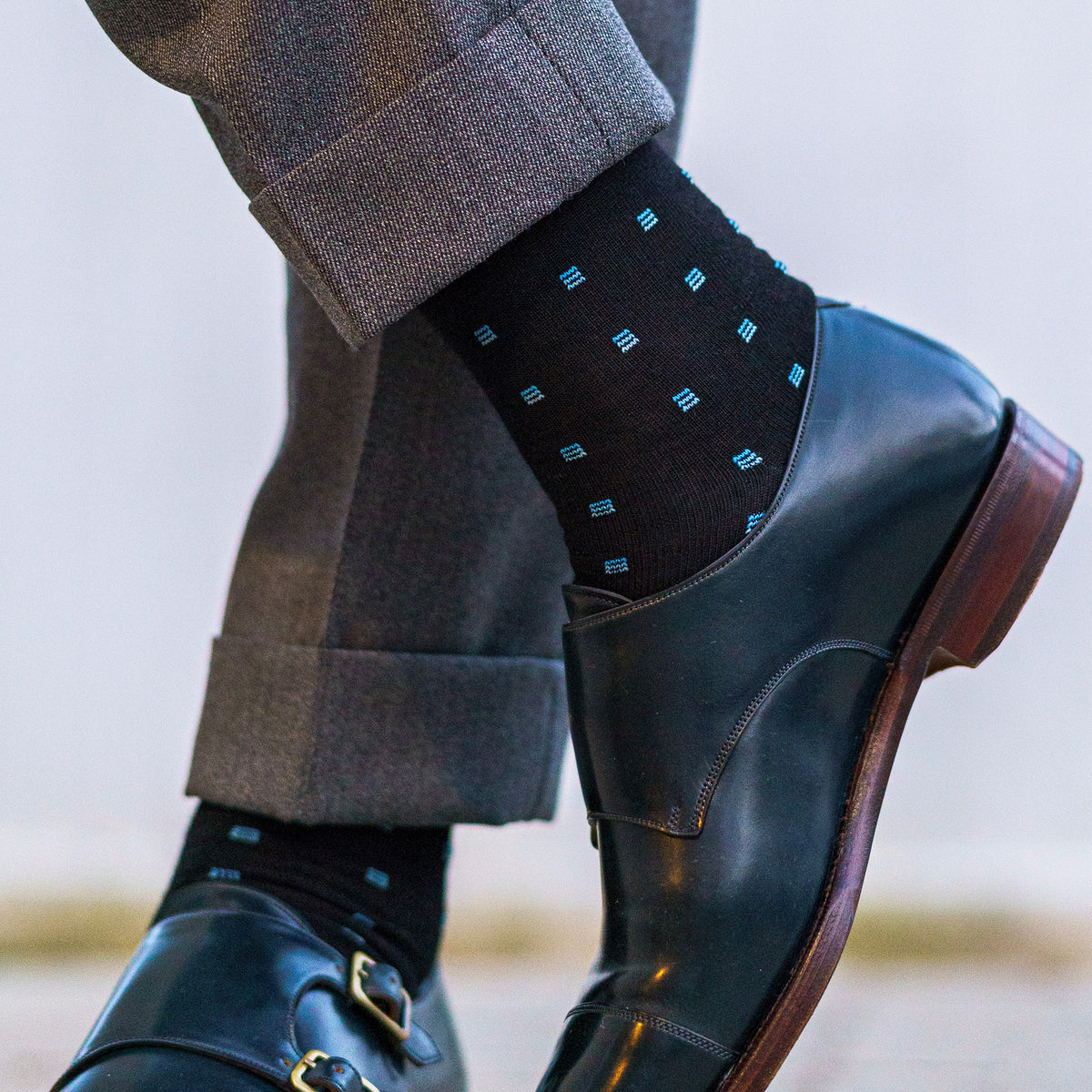 man wearing black wool dress socks decorated with blue geometric patterns paired with blue dress shoes and grey slacks