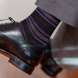 man wearing black dress socks decorated with purple and grey horizontal stripes crossing legs