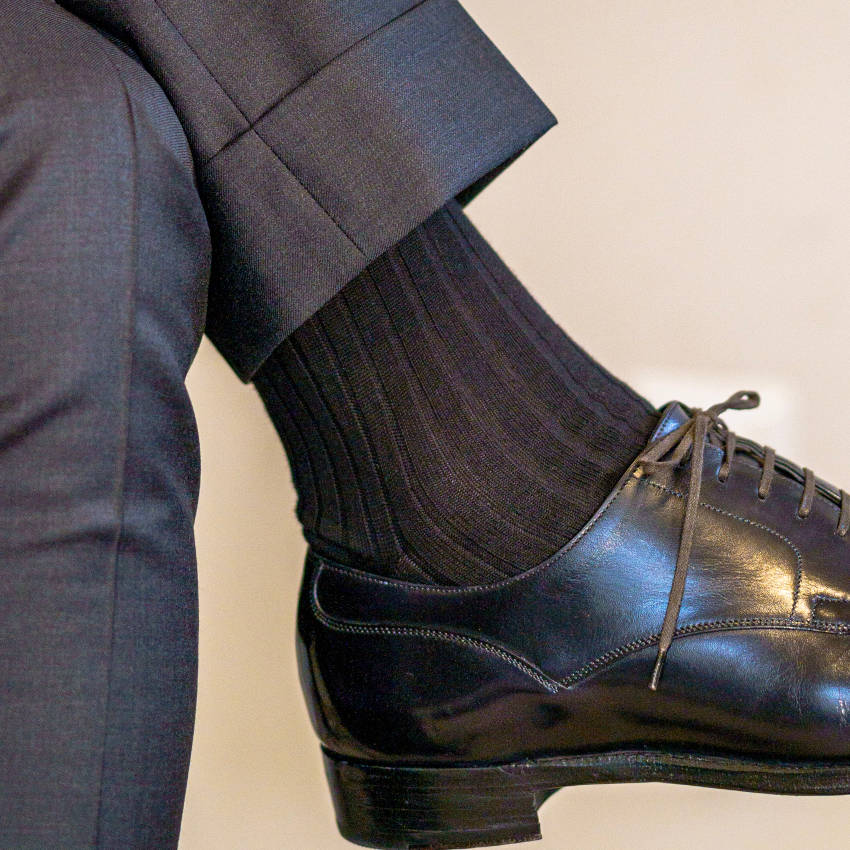 man crossing legs wearing black ribbed dress socks with black oxfords and charcoal trousers
