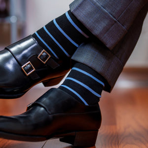man crossing ankles wearing black and light blue striped dress socks with a grey suit