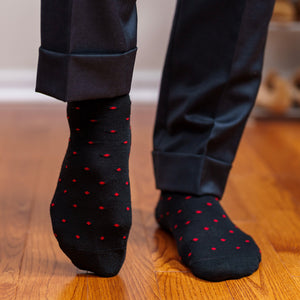 man walking on hardwood floors wearing black dress socks decorated with red dots