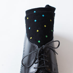 pair of black dress socks decorated with alternating yellow blue and green polka dots rolled up inside black dress shoes