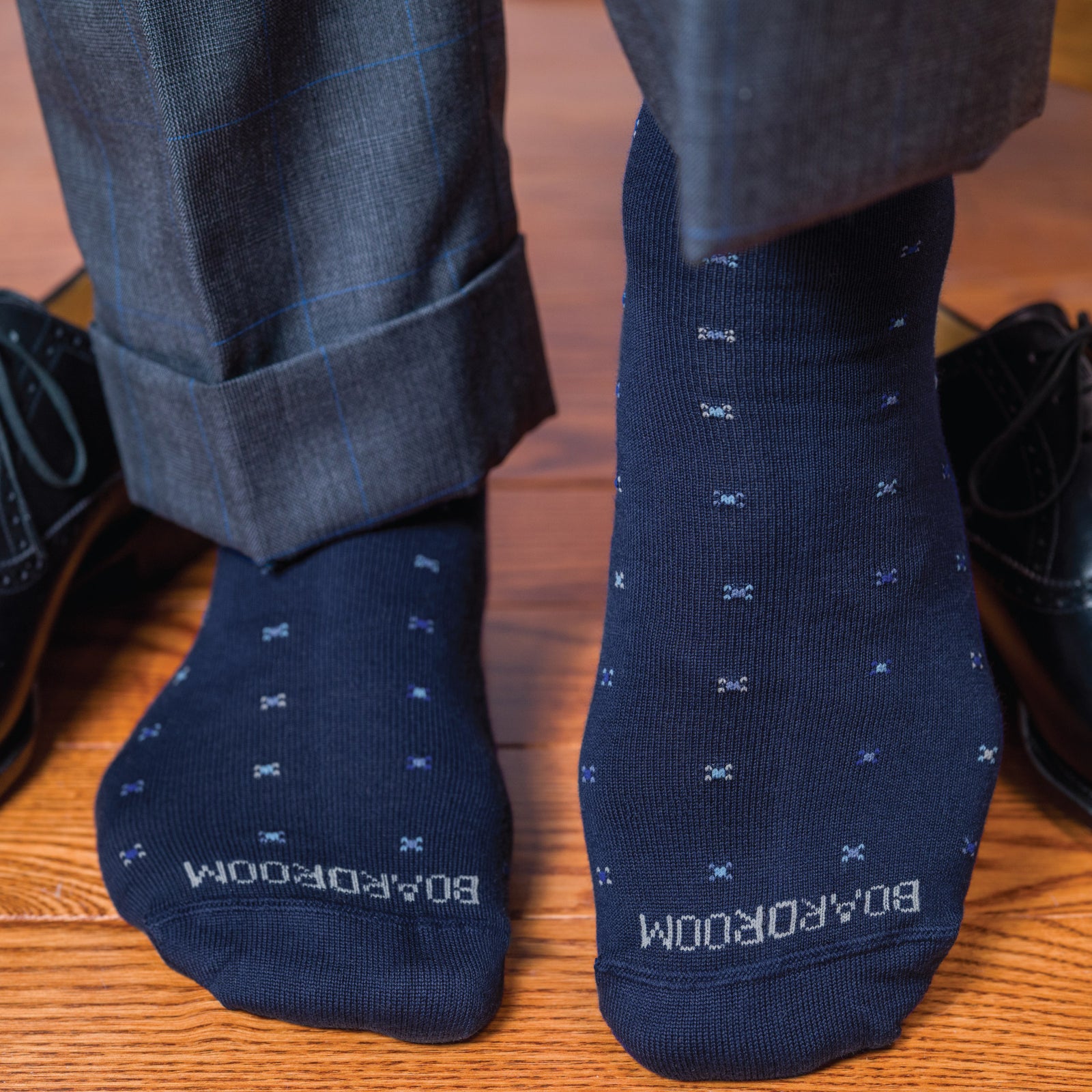 man standing on hardwood floors wearing boardroom socks navy geometric pattern mid calf dress socks