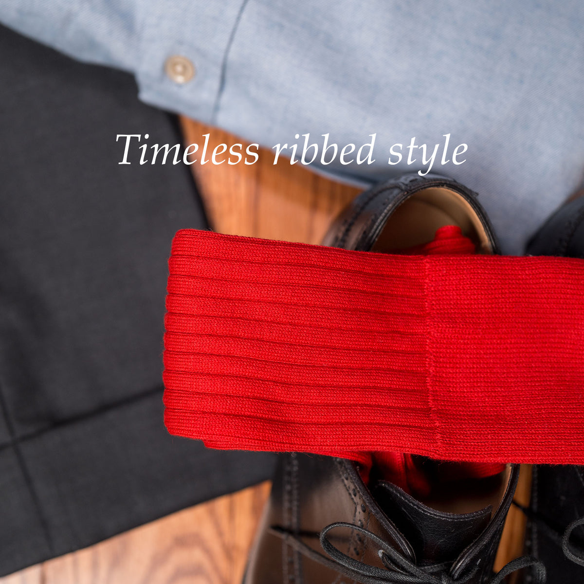 pair of red ribbed dress socks on top of black oxfords alongside charcoal slacks and a blue oxford shirt