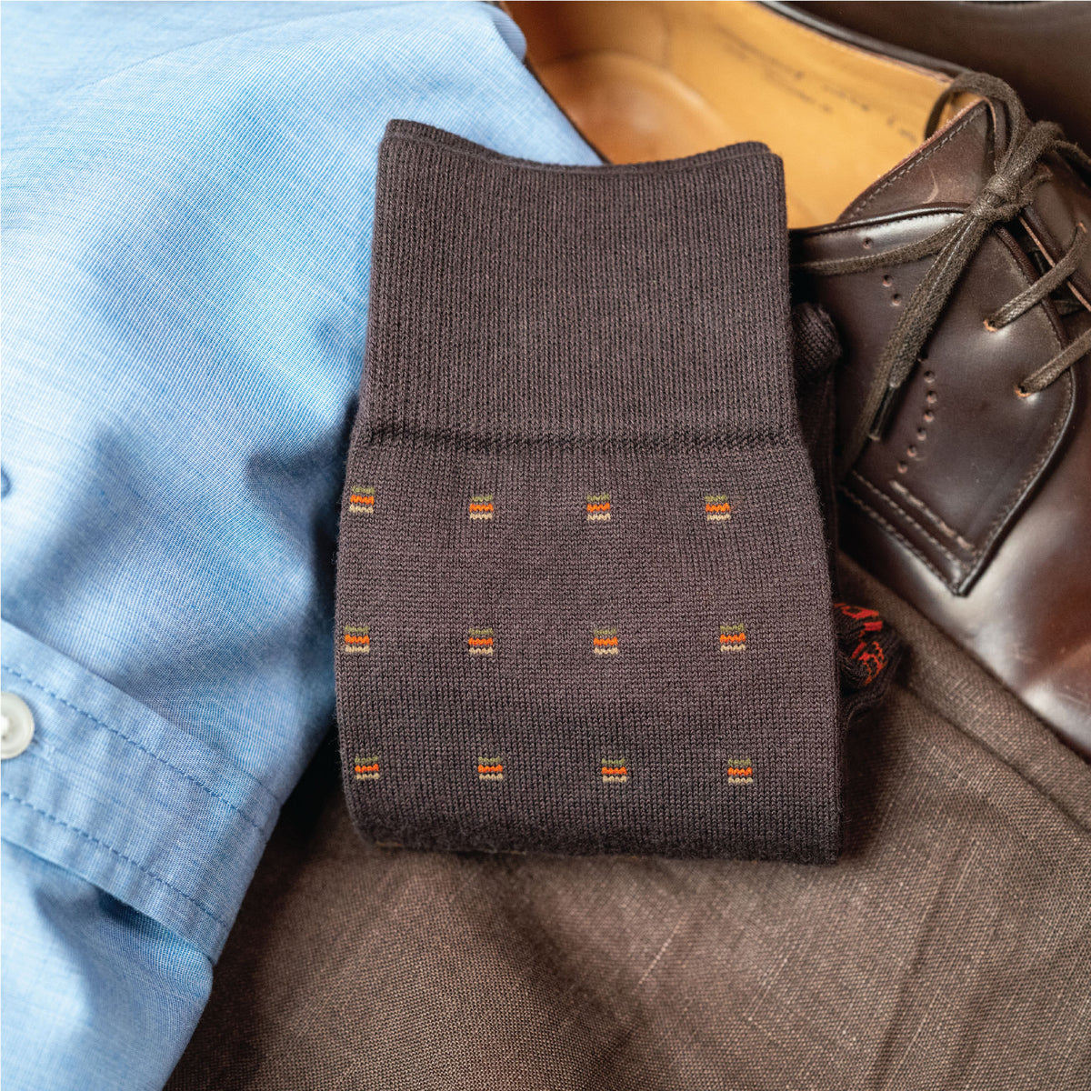 image of brown patterned dress socks laid folded flat on top of pants and shirt and loafers