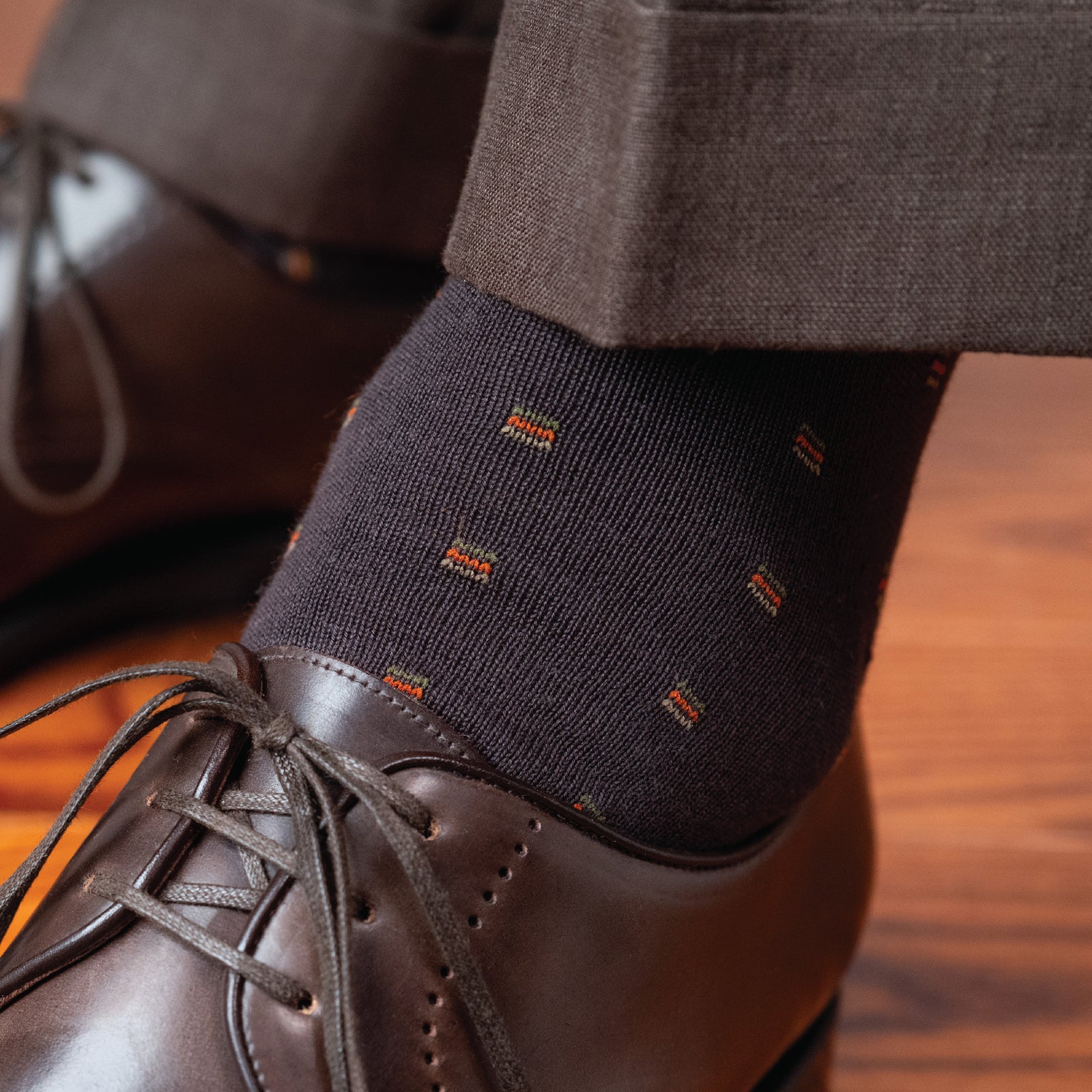 close up detailed image of a brown patterned dress sock on left foot worn with pants and dress shoes