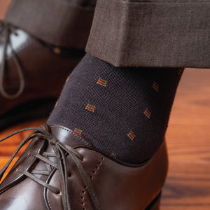 close up detailed image of a brown patterned dress sock on left foot worn with pants and dress shoes
