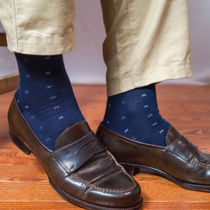 man sitting on stool with his feet on the ground wearing dark brown loafers and navy geometric pattern cotton dress socks