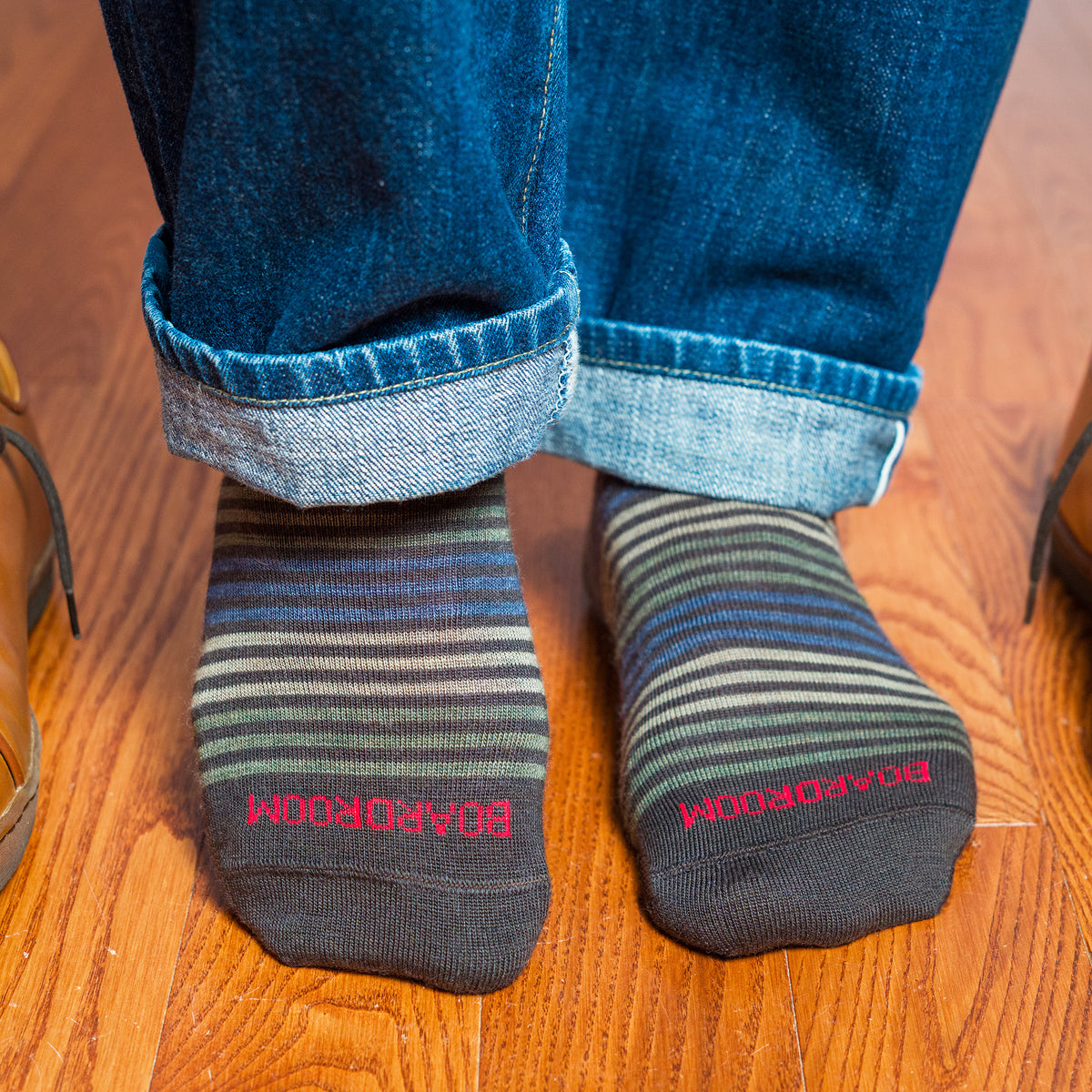 striped dress socks with &#39;BOARDROOM&#39; branding worn with rolled-up jeans on a wooden floor.