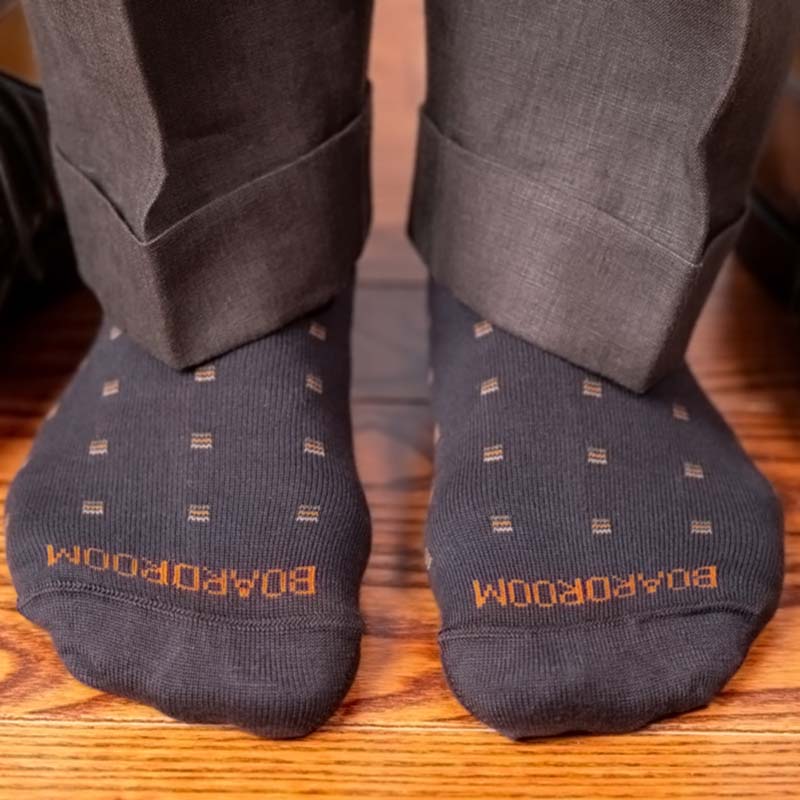 man standing on hardwood floor while wearing brown patterned dress socks with brown trousers
