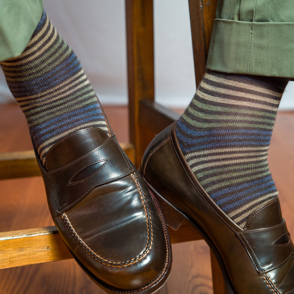 man wearing brown striped dress socks with green slacks and brown penny loafers while seated on stool