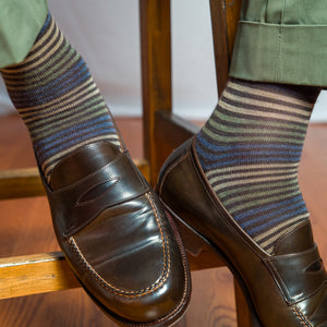man wearing brown striped dress socks with green slacks and brown penny loafers while seated on stool