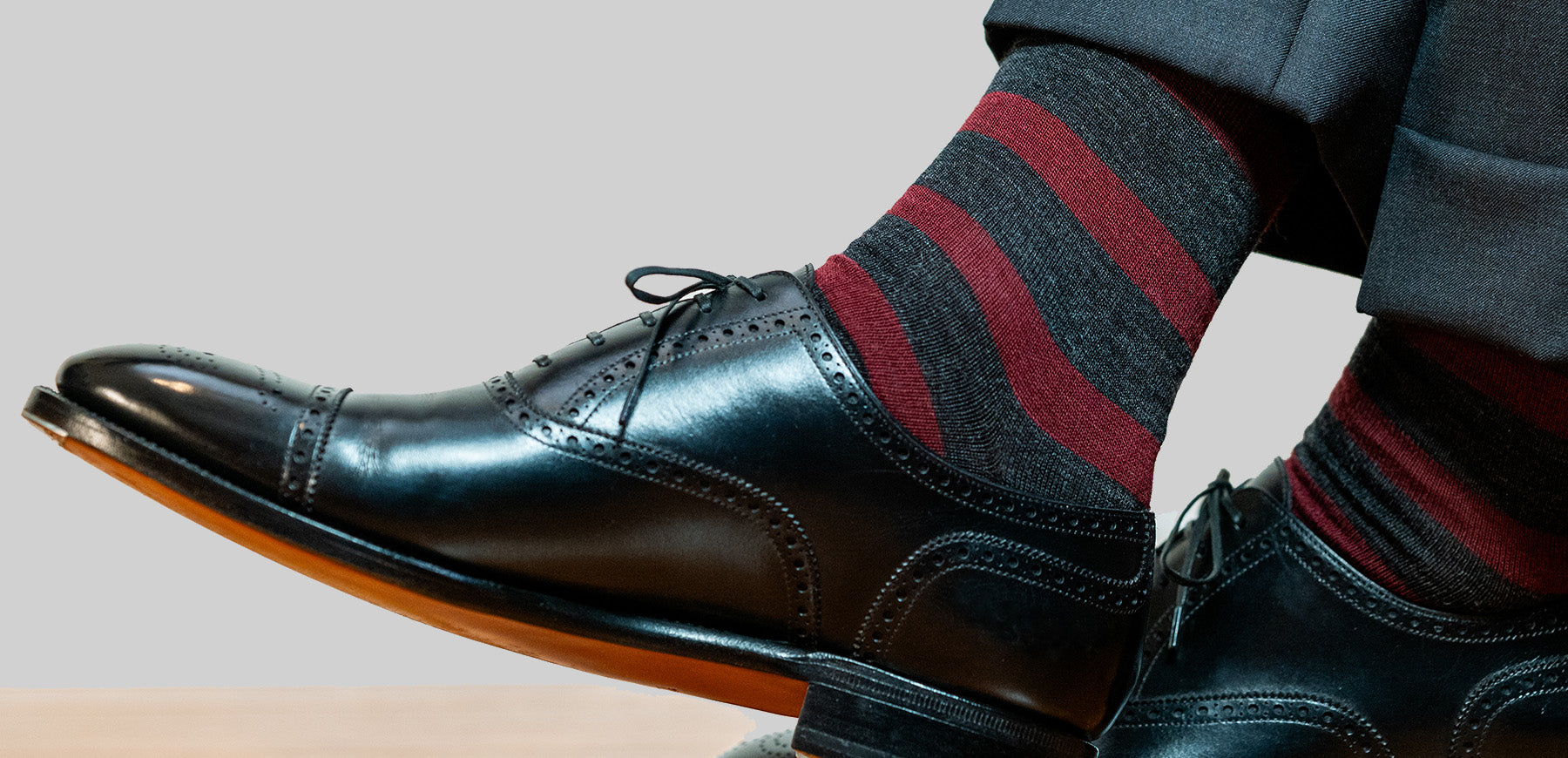 man crossing ankles wearing burgundy and charcoal striped dress socks with black oxfords