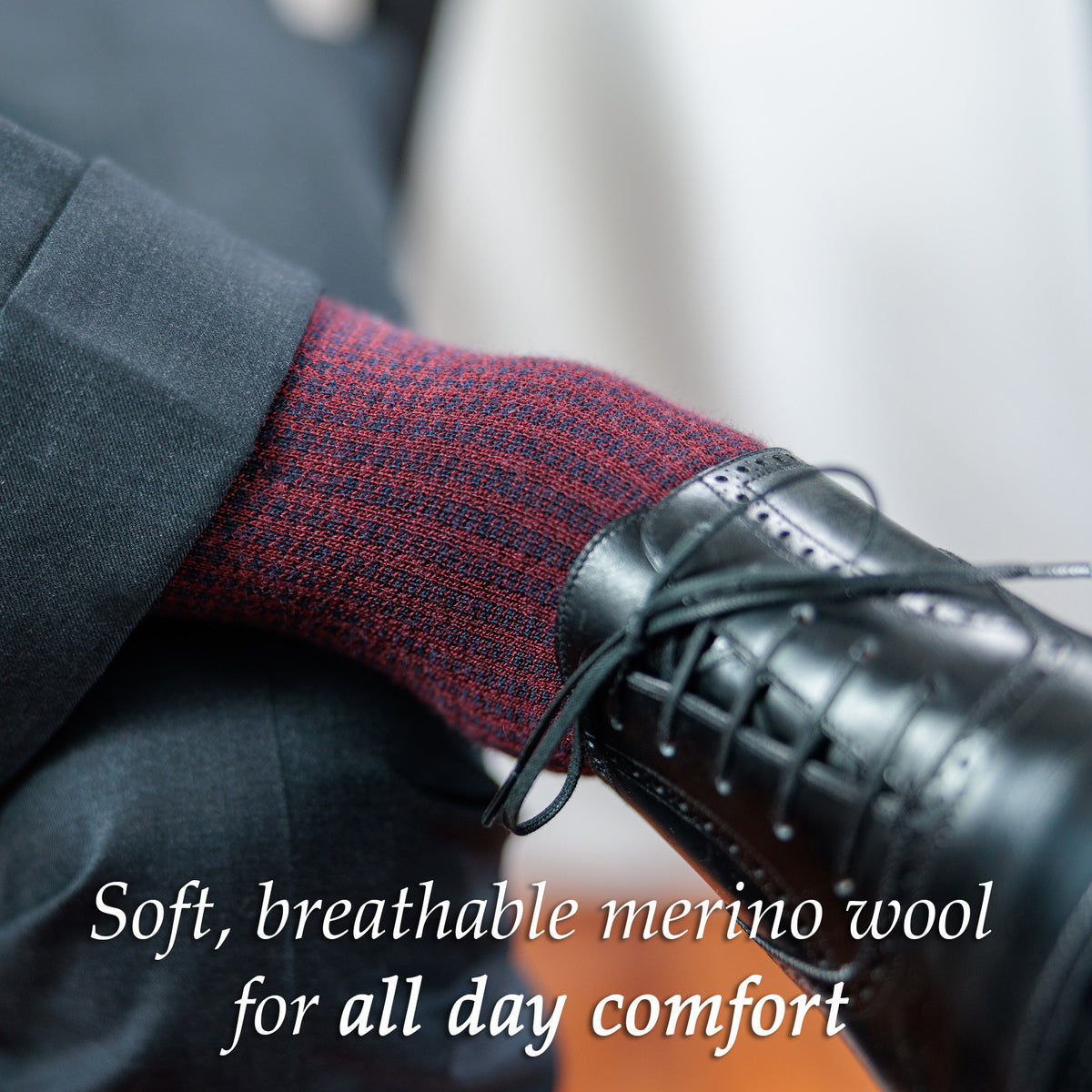man crossing legs wearing navy and burgundy houndstooth dress socks with black oxfords and a charcoal suit