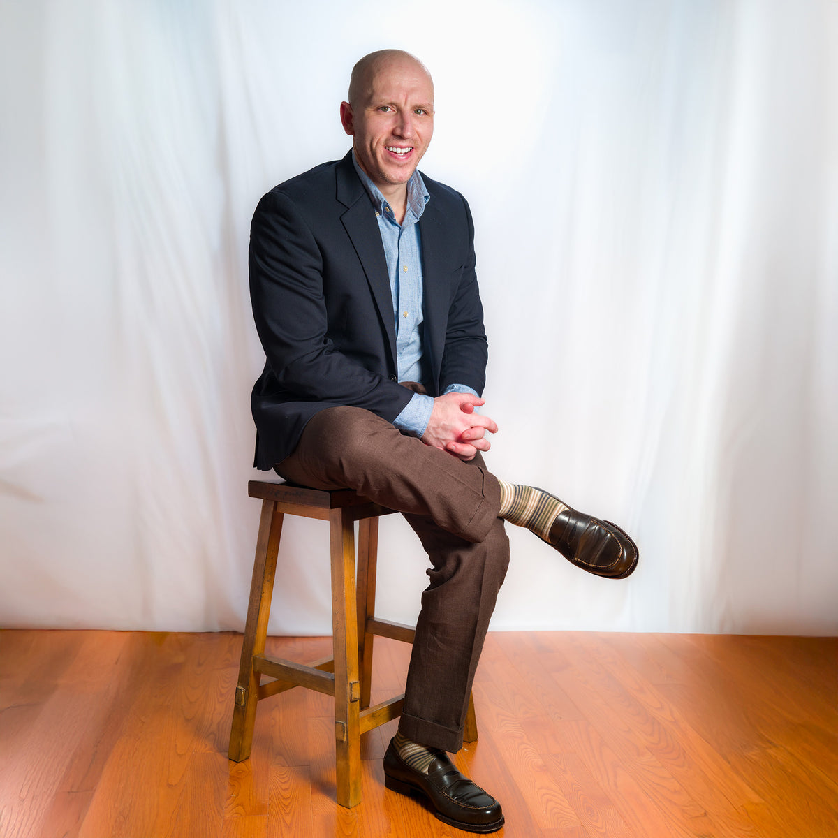 professional man wearing tan Boardroom Socks with business attire sitting on a wooden stool against a white background