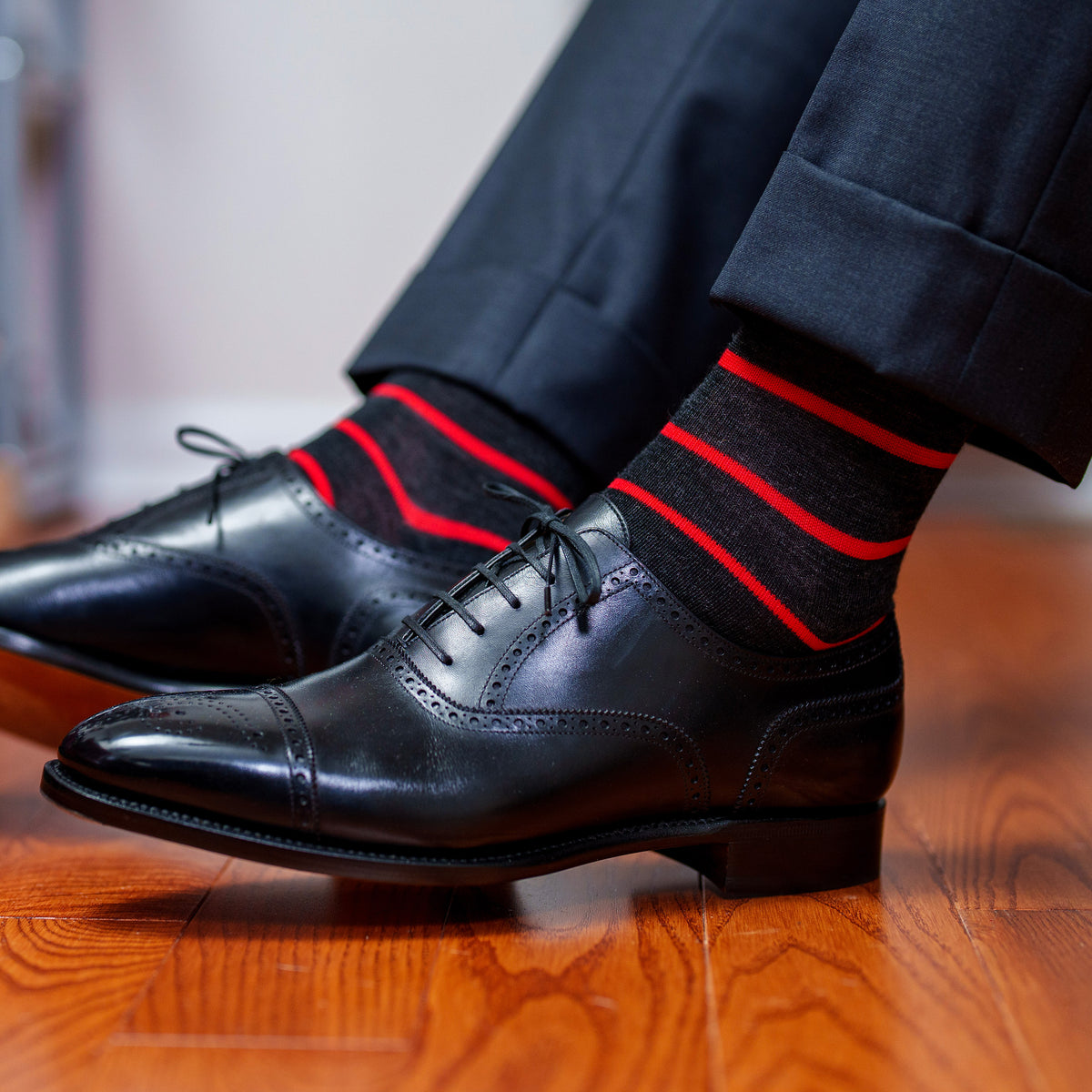 man seated with dark grey suit pants raised up showing charcoal grey dress socks with bright red stripes