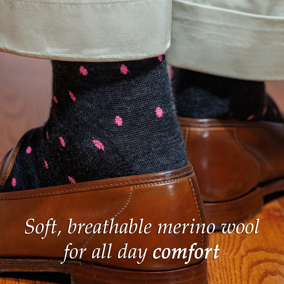 Person wearing dark grey dress socks with pink dots and brown shoes, with text about merino wool comfort.