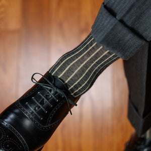 man crossing legs wearing dark grey and tan shadow stripe dress socks with a grey suit and black oxfords