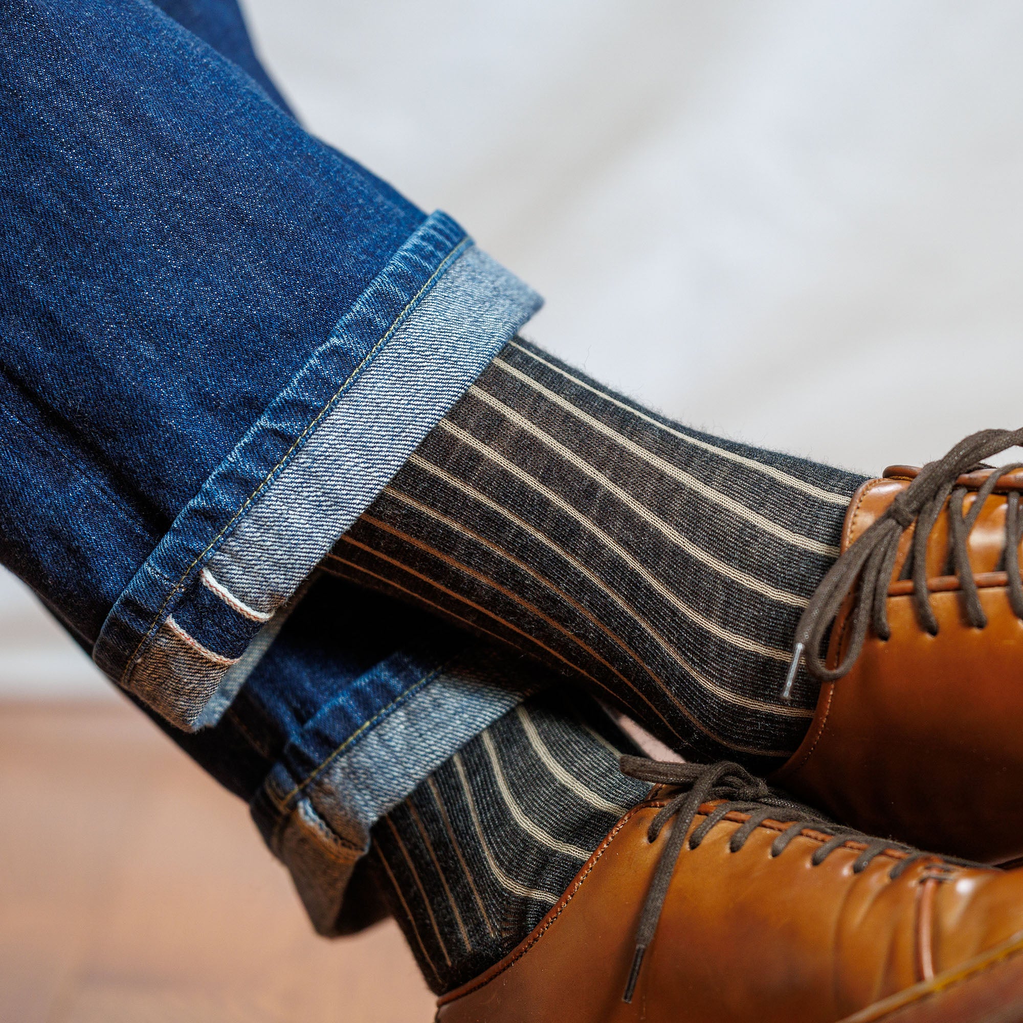 man crossing legs wearing charcoal tan shadow stripe dress socks worn with jeans and brown leather dress sneakers