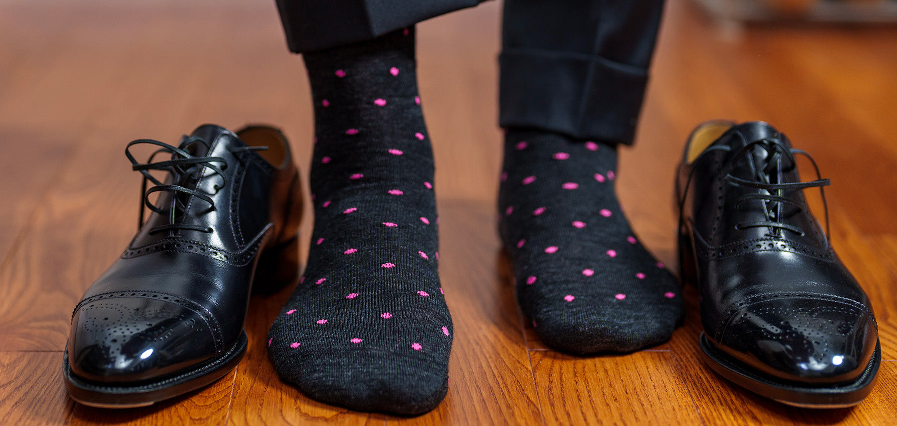 man wearing dark grey wool dress socks decorated with pink dots while standing on hardwood floor with black oxfords