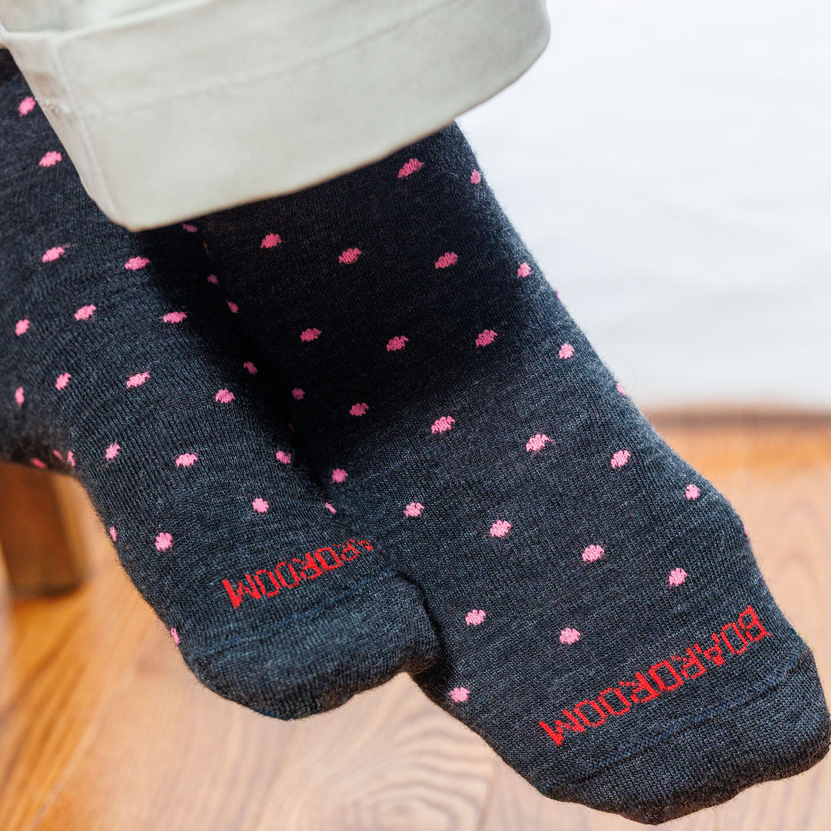 charcoal grey socks with pink polka dots and &#39;Boardroom&#39; branding on a wooden floor.