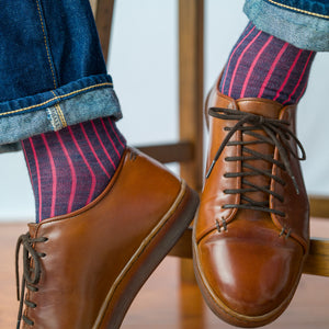 man seated on stool wearing denim blue and coral shadow stripe dress socks with jeans and brown leather sneakers