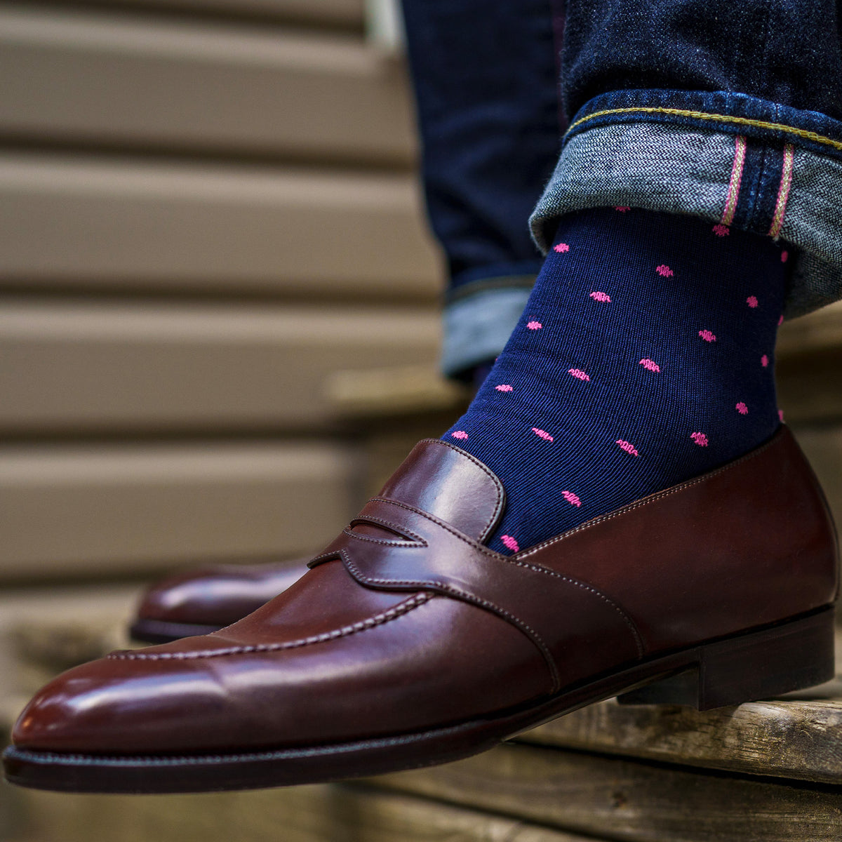 man sitting on stairs wearing dark brown loafers and navy cotton mid-calf dress socks with pink dots