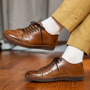 man wearing cream colored dress socks with light yellow trousers and brown leather dress sneakers