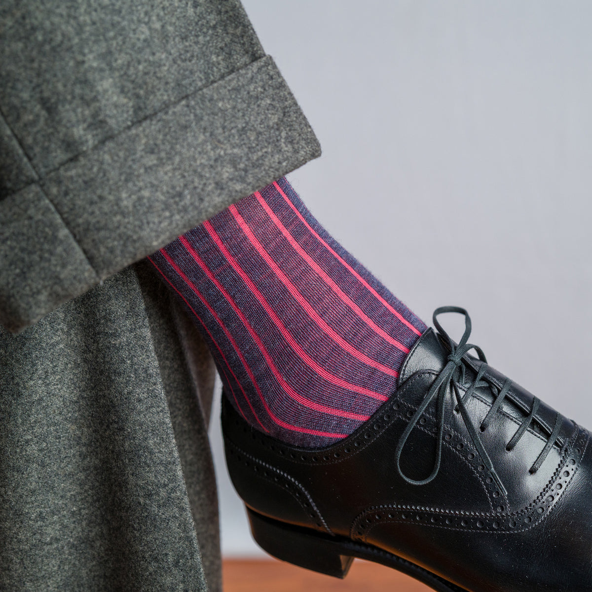 man crossing legs wearing grey slacks with coral and denim shadow stripe dress socks and black oxfords