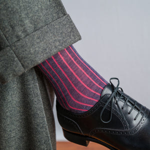 man crossing legs wearing grey slacks with coral and denim shadow stripe dress socks and black oxfords