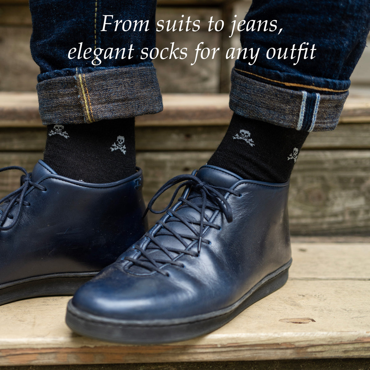 man standing on wooden staircase wearing black skull and crossbone dress socks with jeans and navy blue leather sneakers