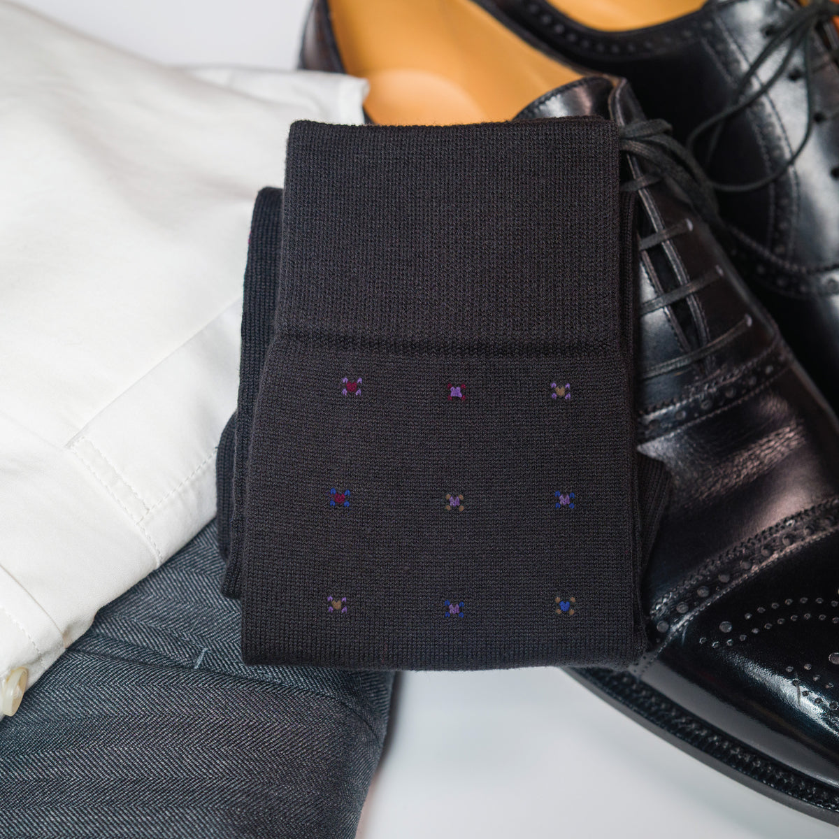 pair of Black Geometric Merino Wool Mid-Calf Dress Socks laying on clothing and shoes