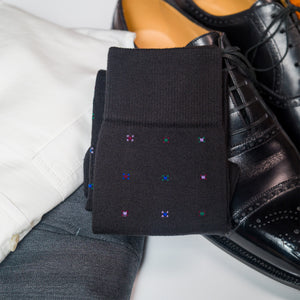 a pair of folded black geometric cotton dress socks on top of clothing and a pair of shoes