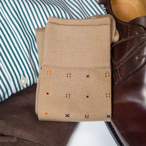a folded pair of khaki geometric pattern dress socks laying on top of clothing and a pair of shoes