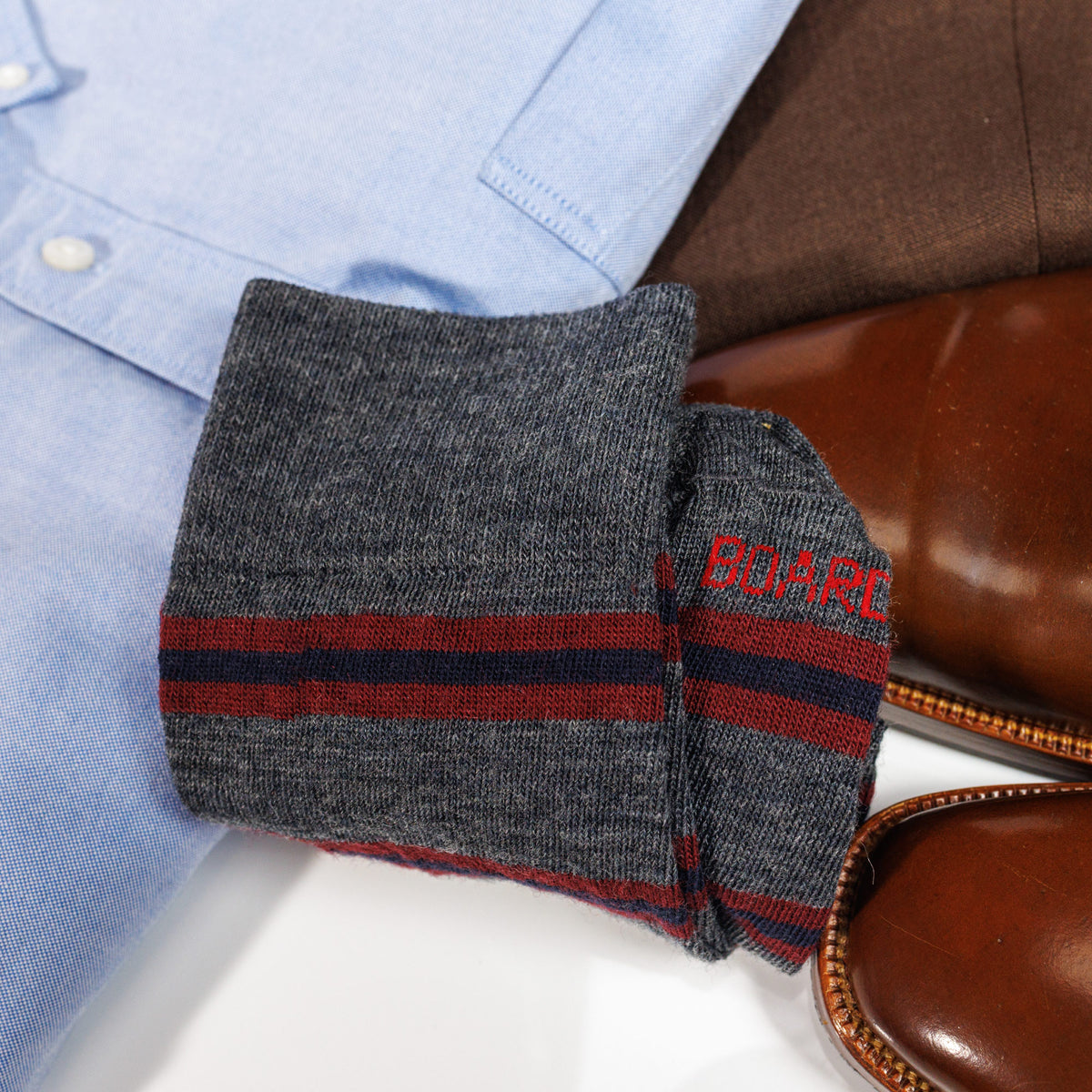 folded pair of Burgundy and Navy Stripes on Grey Merino Wool Over the Calf Dress Socks laying on top of clothing