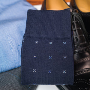 a pair of over the calf navy cotton dress socks with a geometric pattern folded on top of clothing and shoes