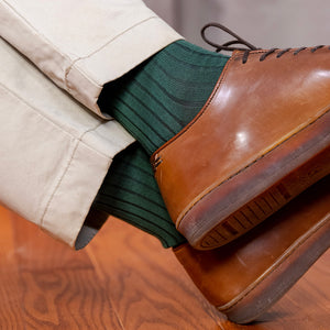 man crossing ankles wearing ribbed forest green dress socks with light khaki chinos and leather dress sneakers