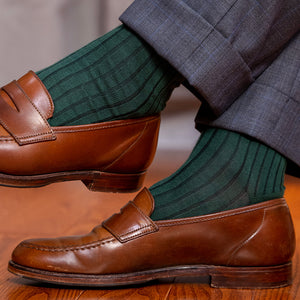 man crossing legs wearing grey windowpane suit trousers with racing green ribbed dress socks and brown penny loafers